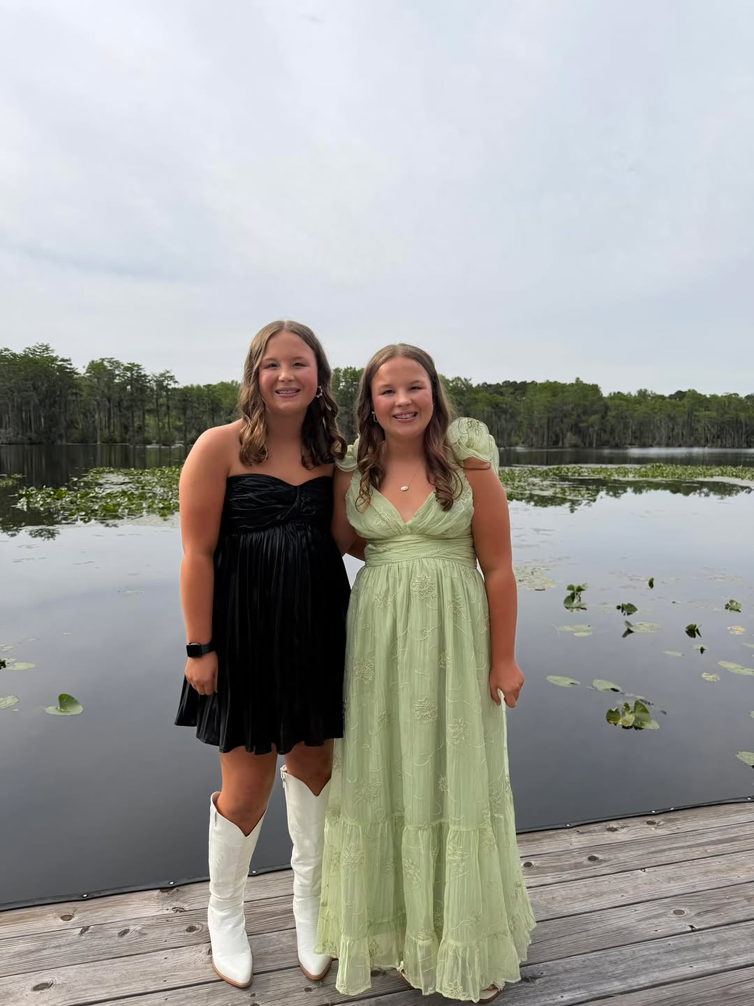 Two friends wearing WPB dresses on a lake dock at golden hour